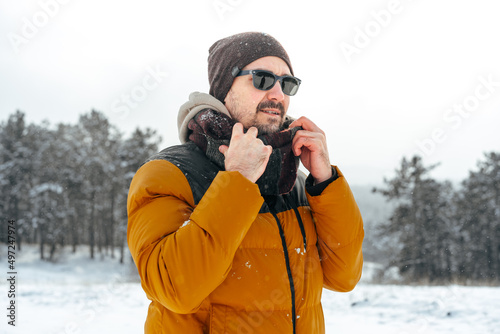 Young man in warm coat standing in snowy winter forest