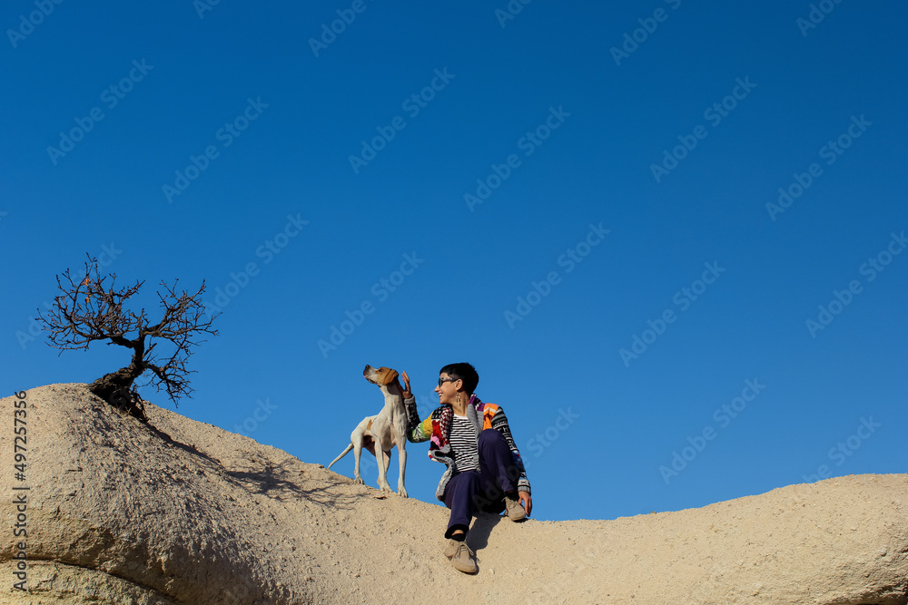 Beautiful smiling female with short hair sitting with her dog on mountain