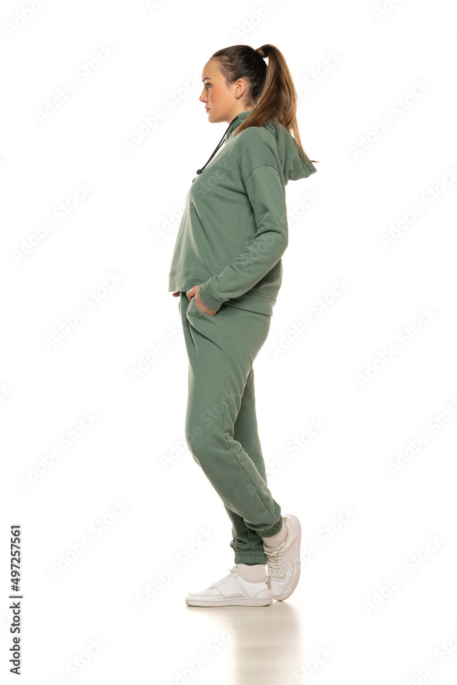 Side view of a young woman in a green tracksuit posing to a white background in the studio Side view of a young woman in a green tracksuit posing to a white background in the studio