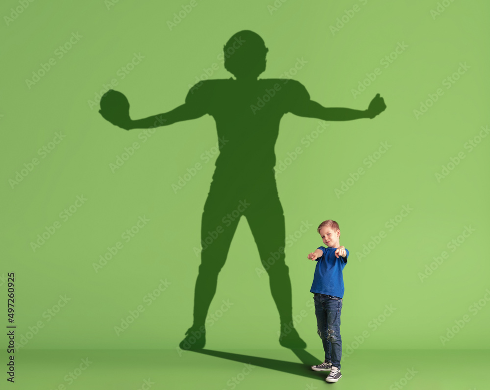 Conceptual image with little kid dreaming about future sport career and shadow of male american football player on green background. Conceptual image with little kid dreaming about future sport career and shadow of male american football player on green background.