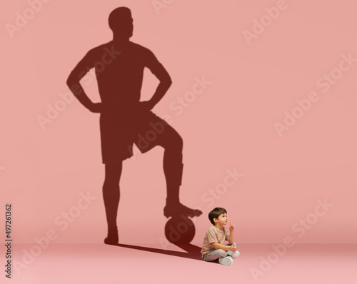 Little boy dreams of becoming a football player isolated on pink background. Childhood and dreams concept. Collage. photo