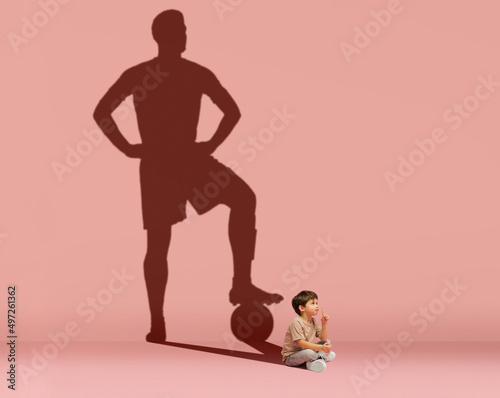 Little boy dreams of becoming a football player isolated on pink background. Childhood and dreams concept. Collage.