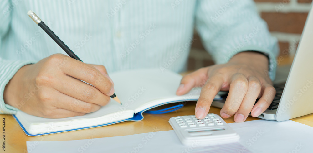 man hand write on notebook and calculate on calculator about debt payment monthly at the table for money management concept