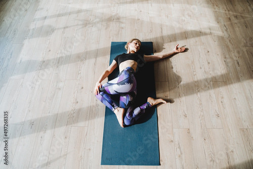 Girl lies on her back doing body twisting, muscle relaxation training, Supta Ardha Matsiendrasana, yoga class top view, blue yoga mat photo