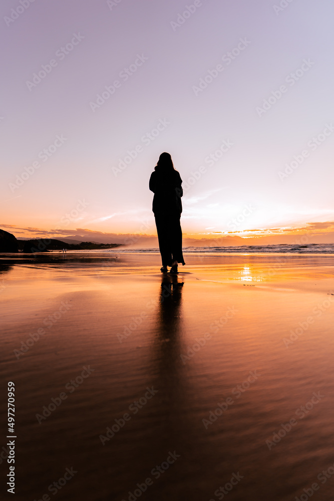 Girl walking barefoot on a beach at sunset