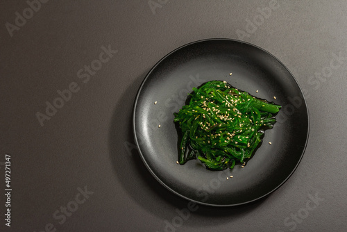 Wakame seaweed salad with sesame seeds and chili pepper in a bowl. Trendy hard light  dark shadow