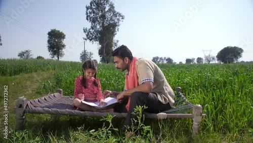 An educated Indian villager helping his daughter with her homework - girl-child education  Beti Bachao Beti Padhao. A young girl with braided hair studying with her father - Indian agriculture  Ind... photo