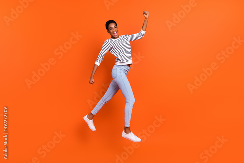 Full length body size view of attractive cheerful slim fit girl jumping running isolated over vivid orange color background