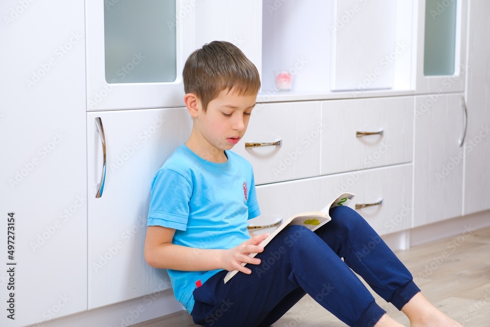 Boy of primary school age teaches lessons and reads a book sitting on the floor. Crafting. Creativity. Back to school. Preparation for school. Classes for children of preschool age. Distance learning. Boy of primary school age teaches lessons and reads a book sitting on the floor. Crafting. Creativity. Back to school. Preparation for school. Classes for children of preschool age. Distance learning.