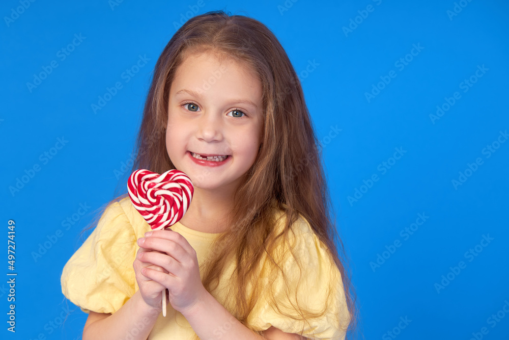 Toothless child. Cute little girl smiles broadly with lollipop  in hands. The first milk tooth fell out. Carefree childhood concept and dental hygiene