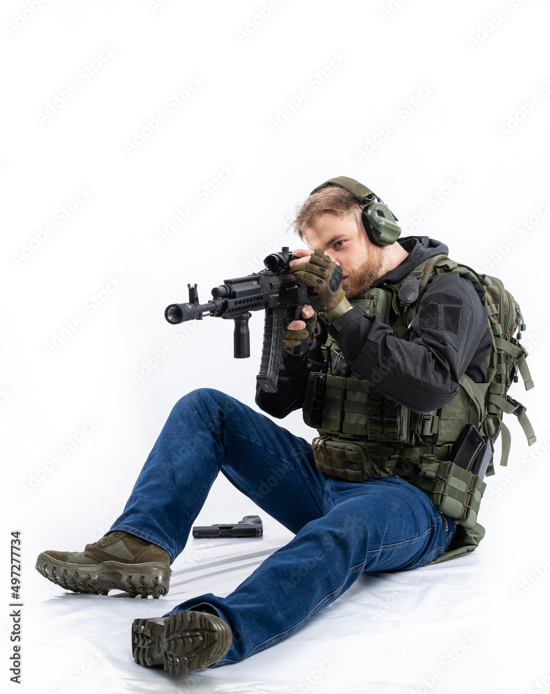 airsoft player in full gear with fire series guns. a man in headphones, a bulletproof vest, with a backpack and a belt, aims his machine gun to the side. profile. White background. airsoft player in full gear with fire series guns. a man in headphones, a bulletproof vest, with a backpack and a belt, aims his machine gun to the side. profile. White background.