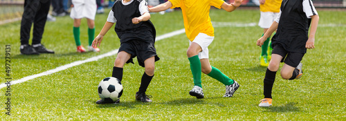 Horizontal image of soccer kids kicking ball on school stadium. Elementary age children play sports. Group of boys in football uniforms compete in tournament match