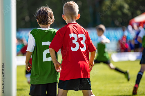 Two Young Boys Comptete in Sports Game. Kids in Opposite Team Standing Side By Side in Red and Green Jersey Shirts. School Kids Play Football in Sunny Summer Day © matimix