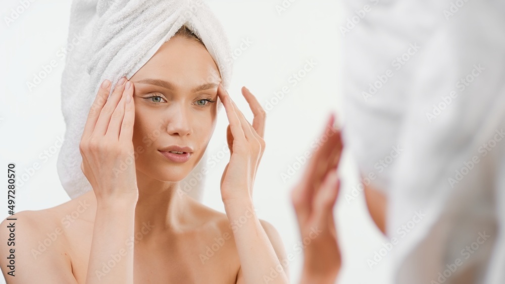 Pretty fit European young woman wrapped in a towel lifts her eyes with her fingers in front of the mirror | Skin care routine concept Pretty fit European young woman wrapped in a towel lifts her eyes with her fingers in front of the mirror | Skin care routine concept