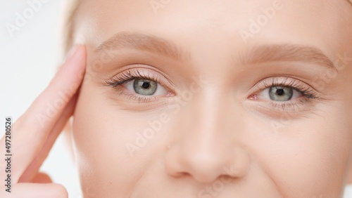 Extreme close-up shot of Caucasian blond female model lifts her eye with her fingers on white background | Droopy eyelids treatment concept