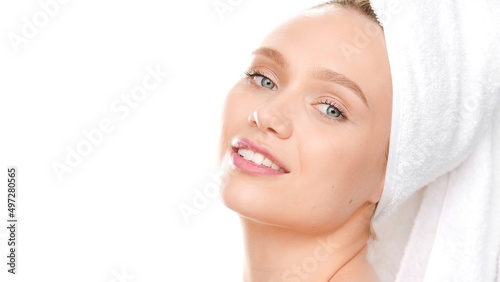 Young attractive woman with towel on her head looks at the camera and smiles inclining her head back on white background   Face care concept