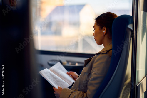 Foto Young female passenger reads book while traveling by train.