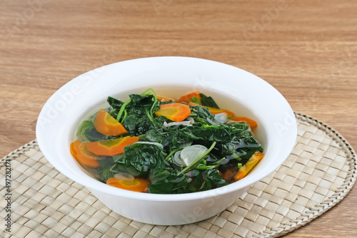 Sayur Bening Bayam, Spinach Clear Vegetable. Indonesian food of spinach, spinach soup with carrots. Served in white bowl on wooden background. 