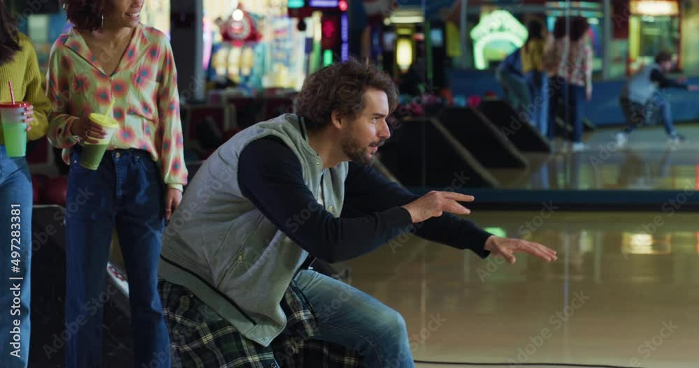 Cinematic shot of happy young male bowler throwing strike ball and exulting victory while having fun to play bowling together with multiracial college friends on weekend in sporting club. Cinematic shot of happy young male bowler throwing strike ball and exulting victory while having fun to play bowling together with multiracial college friends on weekend in sporting club.