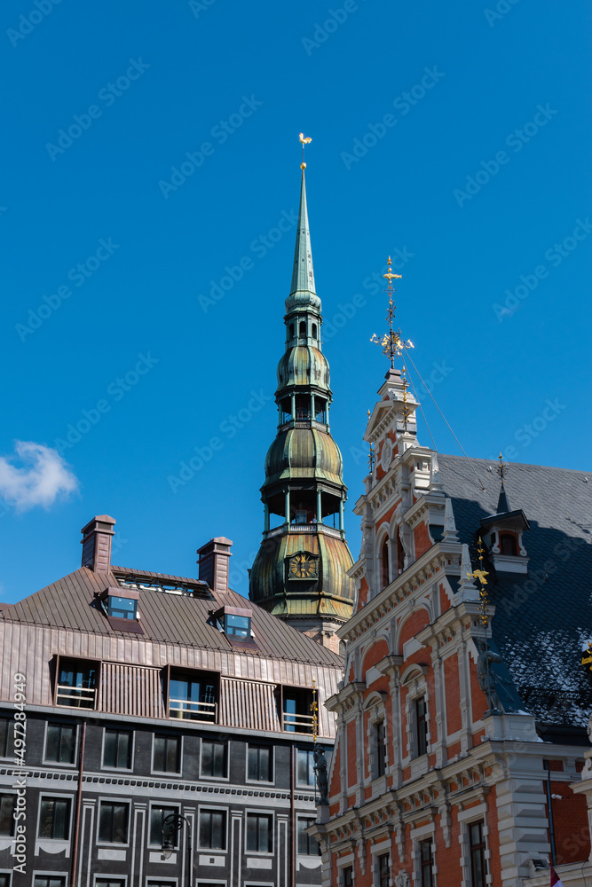 Steeple of St. Peter's Church, behind the House of The Black Heads in Riga, Latvia with blue sky in the background