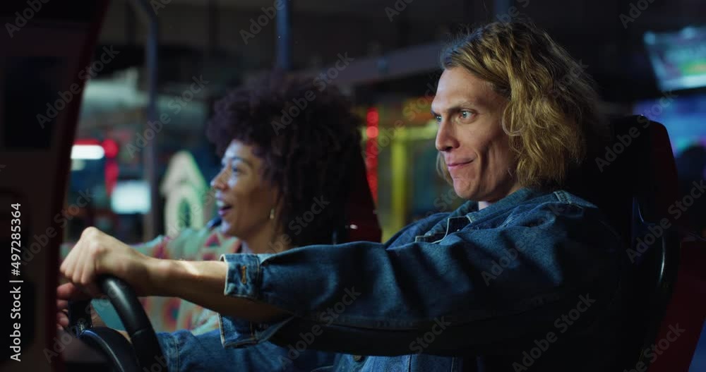 Cinematic shot of young happy interracial couple steering wheel racing in sports car while having fun to play simulation race game together in amusement park on weekend. Cinematic shot of young happy interracial couple steering wheel racing in sports car while having fun to play simulation race game together in amusement park on weekend.