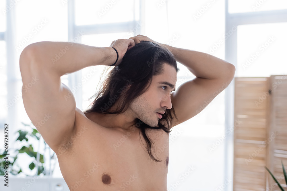 side view of muscular man styling long hair in bathroom. side view of muscular man styling long hair in bathroom.
