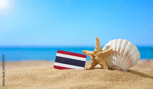 Tropical beach with seashells and Thailand flag. The concept of a paradise vacation on the beaches of Thailand.
