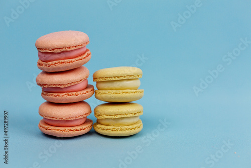 Fototapeta Naklejka Na Ścianę i Meble -  Towers of macaroni cakes in yellow and pink pastel tones on a blue background. culinary concept. Delicious multicolored macaroons.