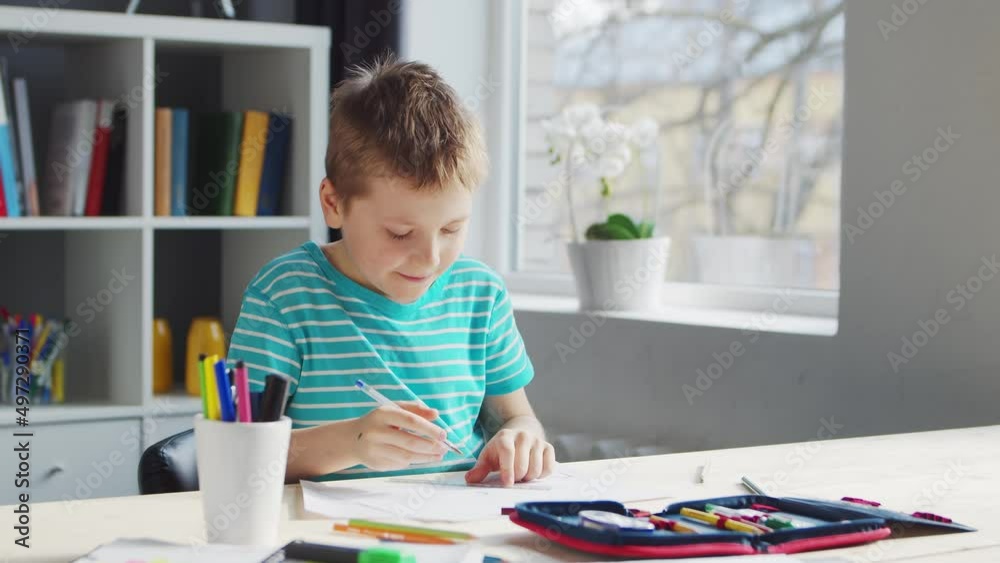 Boy is Doing his Homework at the Table. Cute Child is Learning at Home with the Help of Textbooks and School Materials. Study and Education Concept. Boy is Doing his Homework at the Table. Cute Child is Learning at Home with the Help of Textbooks and School Materials. Study and Education Concept.
