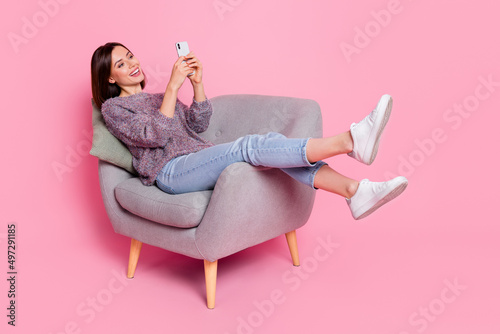 Portrait of attractive cheerful girl in armchair using device gadget smm isolated over pink pastel color background photo