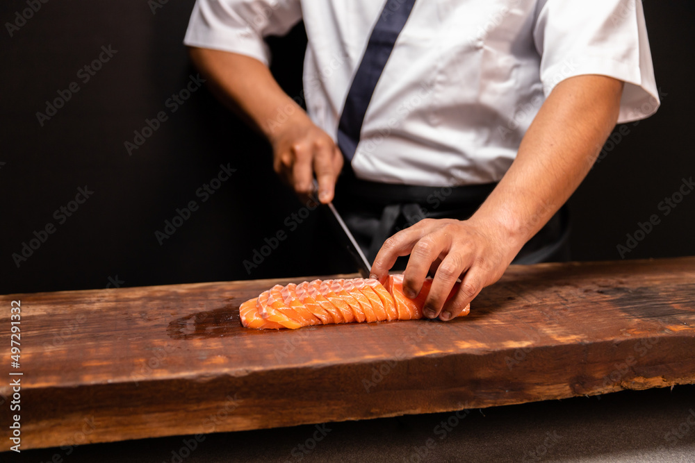 Chef's hand holding fresh piece of salmon.Closeup of chef hands preparing japanese food. Japanese chef making sushi at restaurant.Chef making traditional japanese sushi on wood board.