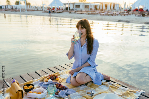 Beautiful woman in sea style sitting on wooden bridge drinking wine at sunset. Travel and Vacation. Freedom Concept.