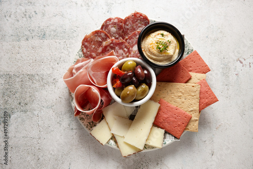 top shot of an antipasto platter on a white table with olives, cheese, cold cuts, and hummus
