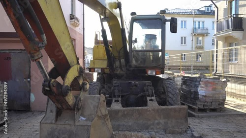 The excavator stands motionless on the construction site. Repair of the sidewalk in the city, replacement of paving slabs, restoration of the infrastructure of the city. Large construction equipment.