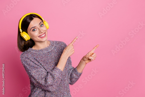 Photo of shiny charming lady dressed sweater earphones pointing empty space isolated pink color background