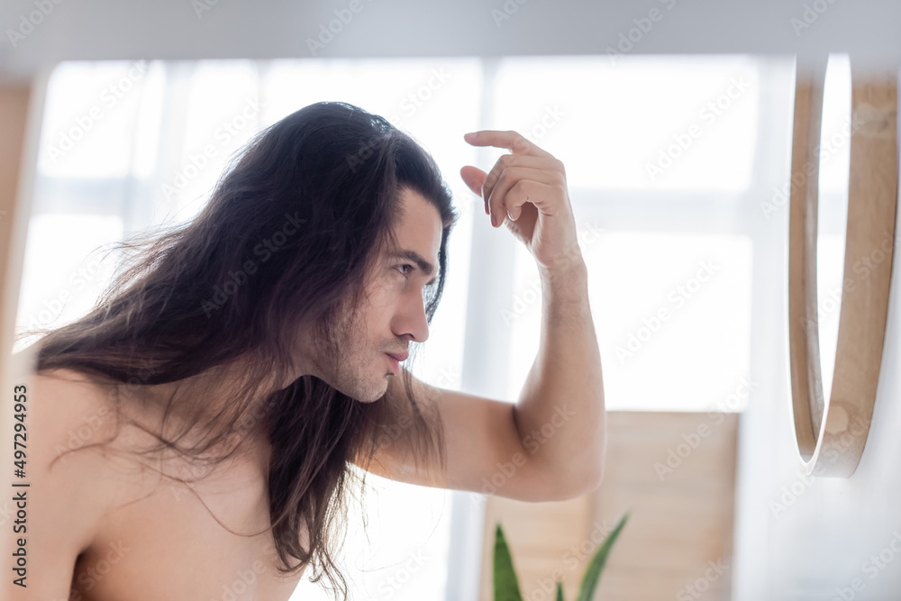 side view of shirtless man styling long hair near mirror. side view of shirtless man styling long hair near mirror.