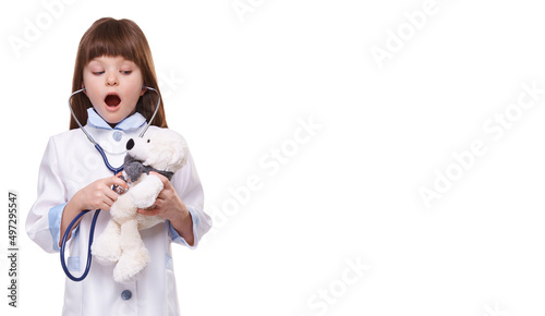 Smiling cute caucasian girl playing doctor and listening teddy bear with stethoscope isolated on white background
