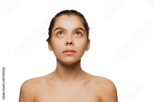 Close-up portrait of young beautiful girl with no makeup looking upwards isolated over white studio background. Natural beauty concept.