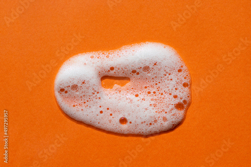 Foam swatch on an orange background. Soapy liquid texture with bubbles. Natural sunshine and shadows. Skin care cleansing cosmetic in top view.