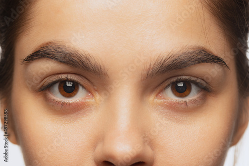 Cropped close-up image of female beautiful brown eyes looking at camera isolated over white studio background