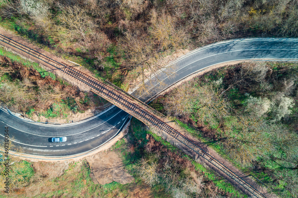 Obraz premium Top aerial view of a railway rails over a bridge and a beautiful forest. Landscape of a road and driving car