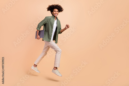 Full length body size view of attractive cheery guy jumping holding laptop running work isolated on beige pastel color background