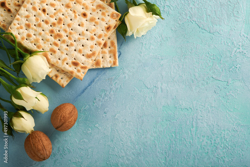 Passover celebration concept. Matzah, red kosher walnut and spring beautiful rose flowers. Traditional ritual Jewish bread on light turquoise or blue background. Passover food. Pesach Jewish holiday.