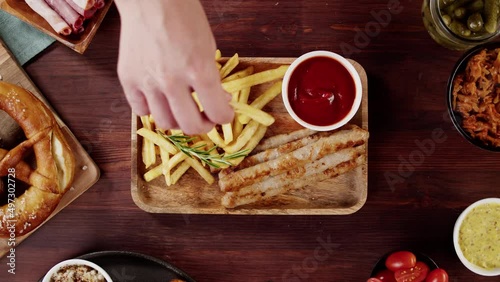 Putting tray with smoked sasuages and fried potatoes top view, pickled cucumbers, bratwursts and fresh pretzels on table. Traditional German Cuisine. Composition of Cooked National Czech Food.  photo