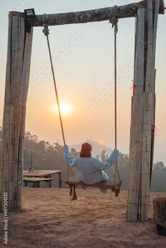 Loneliness woman sitting on the swing and looking at the sun at sunrise time.
