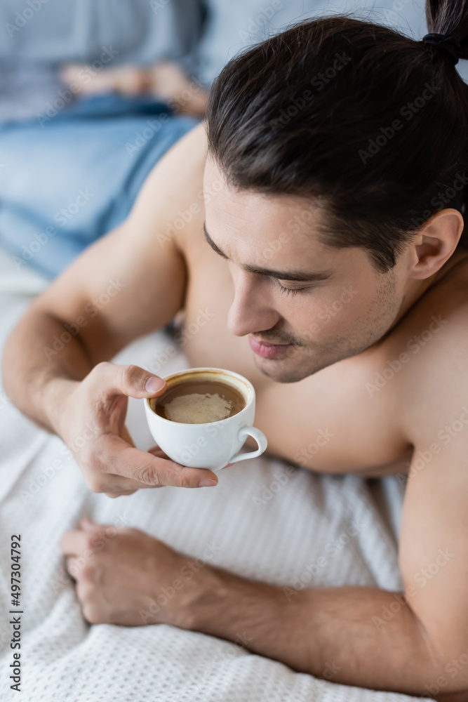 overhead view of shirtless man holding cup of coffee.