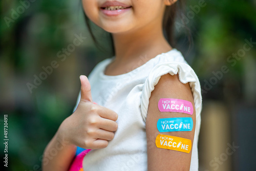 Asian young girl showing her arm with multicolored bandage after got vaccinated or inoculation, child immunization.