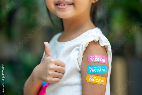 Asian young girl showing her arm with multicolored bandage after got vaccinated or inoculation, child immunization. photo