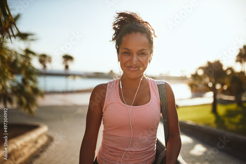 Fototapeta Sporty woman standing on a promenade carrying a yoga mat