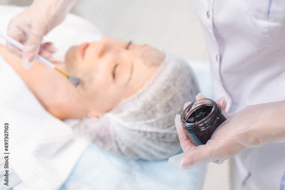 Hands of cosmetology specialist applying carbon nanogel on young woman patient face using brush, getting ready for carbon peeling procedures Hands of cosmetology specialist applying carbon nanogel on young woman patient face using brush, getting ready for carbon peeling procedures